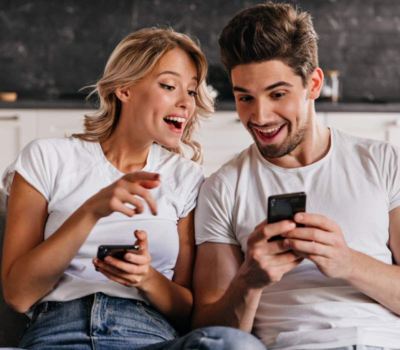 Um casal usando o celular com entusiasmo, simbolizando a experiência de assistir a filmes, séries e canais ao vivo diretamente no Android. O UniTV APK pode ser instalado facilmente no celular, oferecendo entretenimento portátil de alta qualidade, sem complicações. Casal sorridente usando o celular juntos, representando o uso do aplicativo UniTV no smartphone.
