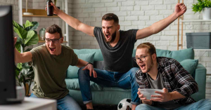 Grupo de amigos comemorando enquanto assistem futebol ao vivo na TV em casa.