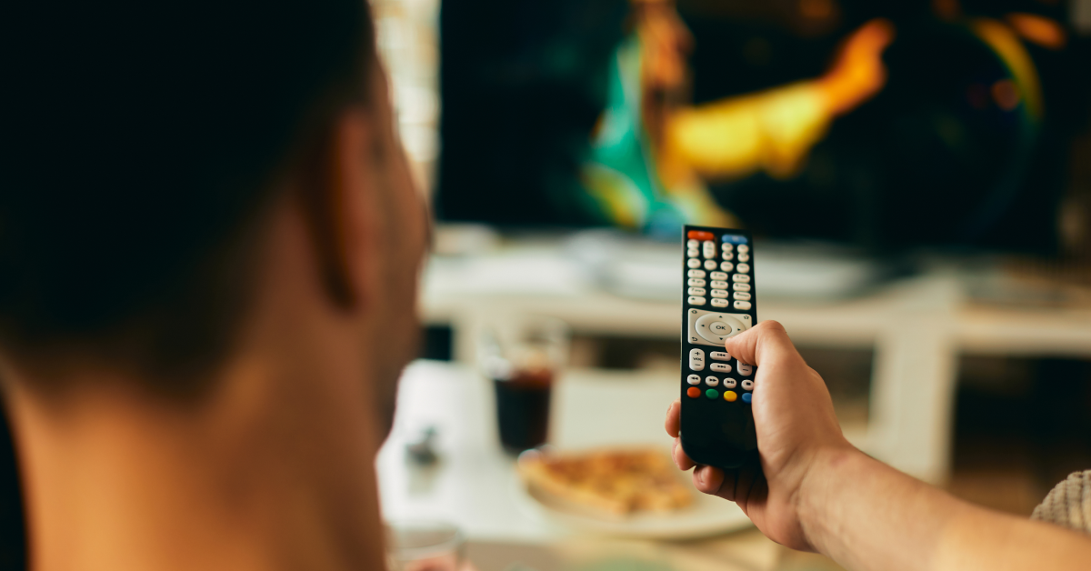 Homem sentado em frente a uma TV com várias opções de canais e filmes exibidos na tela, simbolizando a variedade de conteúdo oferecida pela UniTV.