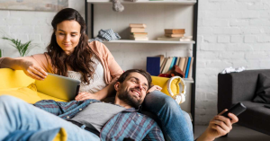Casal relaxando no sofá enquanto assiste conteúdos por IPTV em diferentes dispositivos.