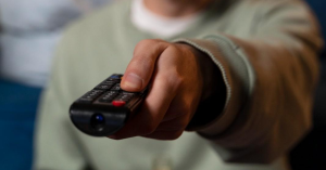 Pessoa segurando controle remoto para trocar de canal na TV.
