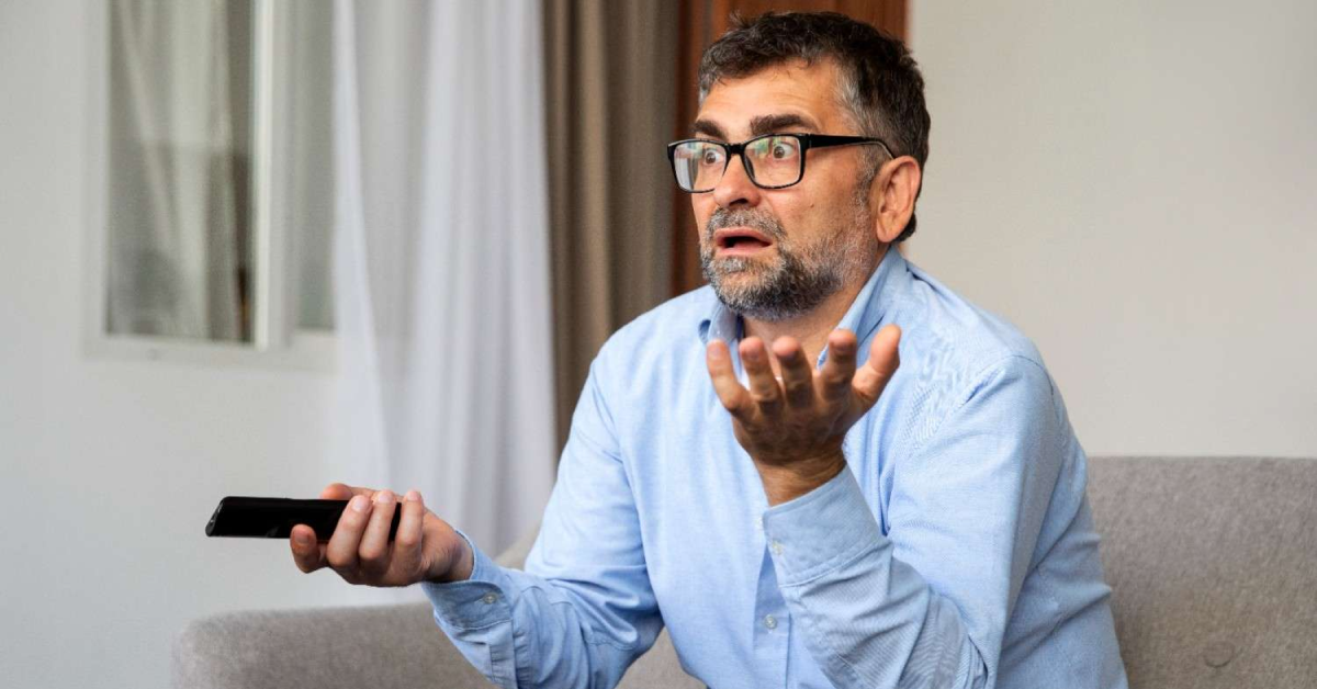 Homem confuso segurando controle remoto, ilustrando frustração com IPTV travando.