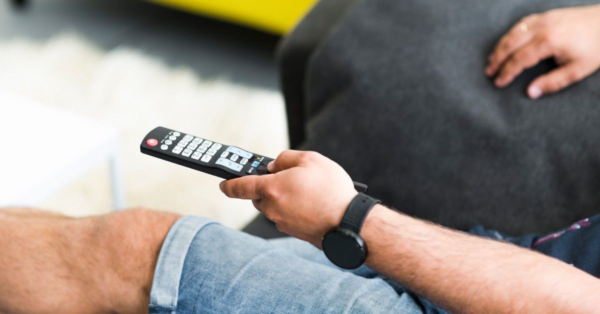 Pessoa segurando controle remoto enquanto assiste TV, representando o uso de aplicativos IPTV no Brasil.